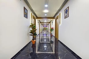 Un pasillo de hotel con suelo de mármol pulido, plantas en macetas y cuadros en las paredes.