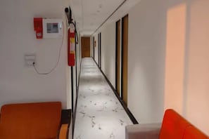 A corridor with a fire extinguisher mounted on the wall, a power outlet, and a door at the end. - FabHotel Januson (Gandhinagar)