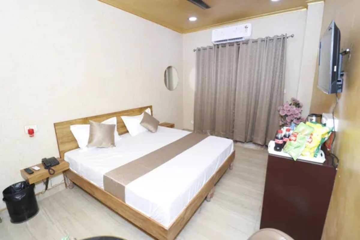 A hotel room with a bed, a desk with a telephone, a trash bin, and a TV on a stand.