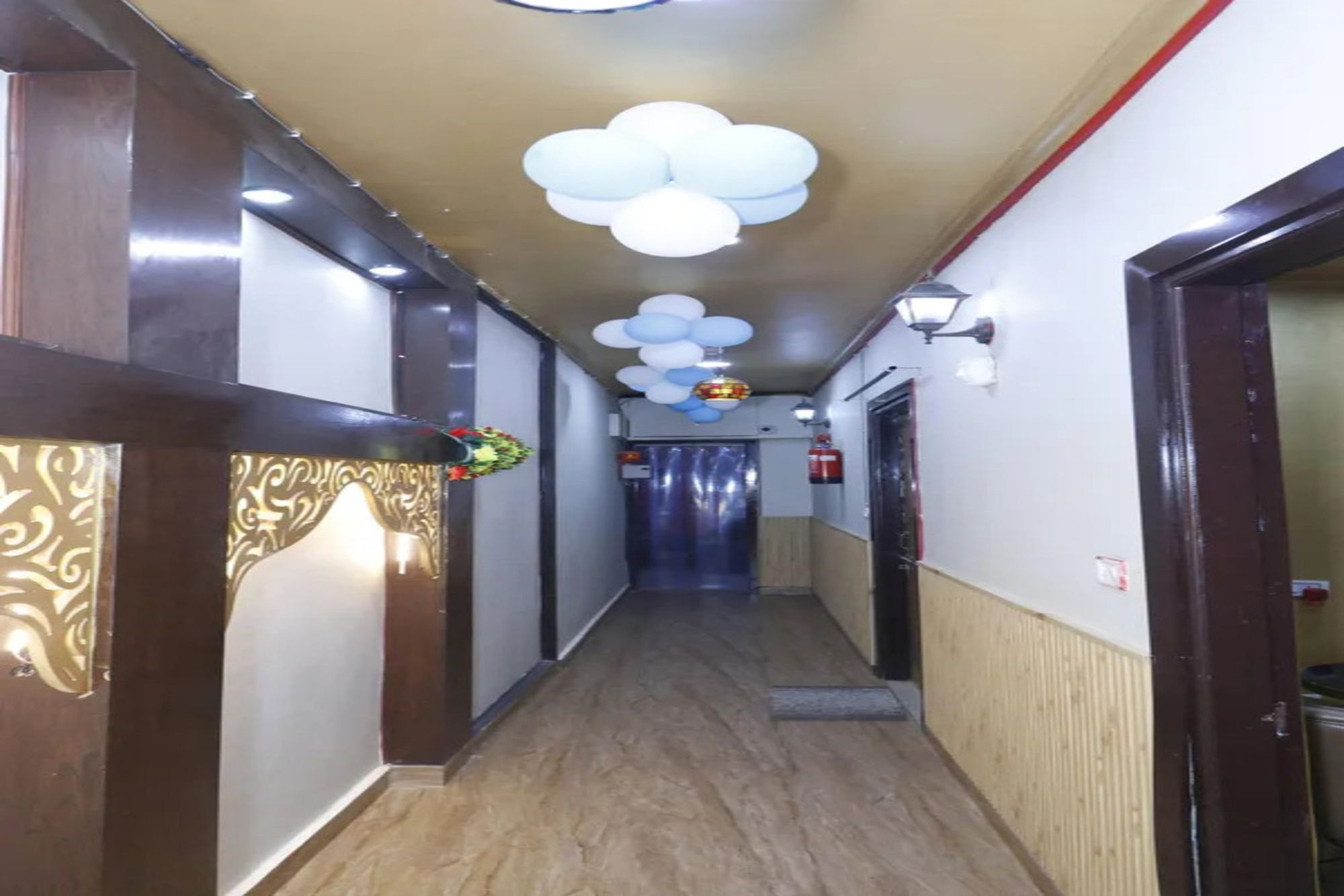 Un pasillo con piso de madera, una pared decorativa a la izquierda y un techo con luces esféricas blancas.