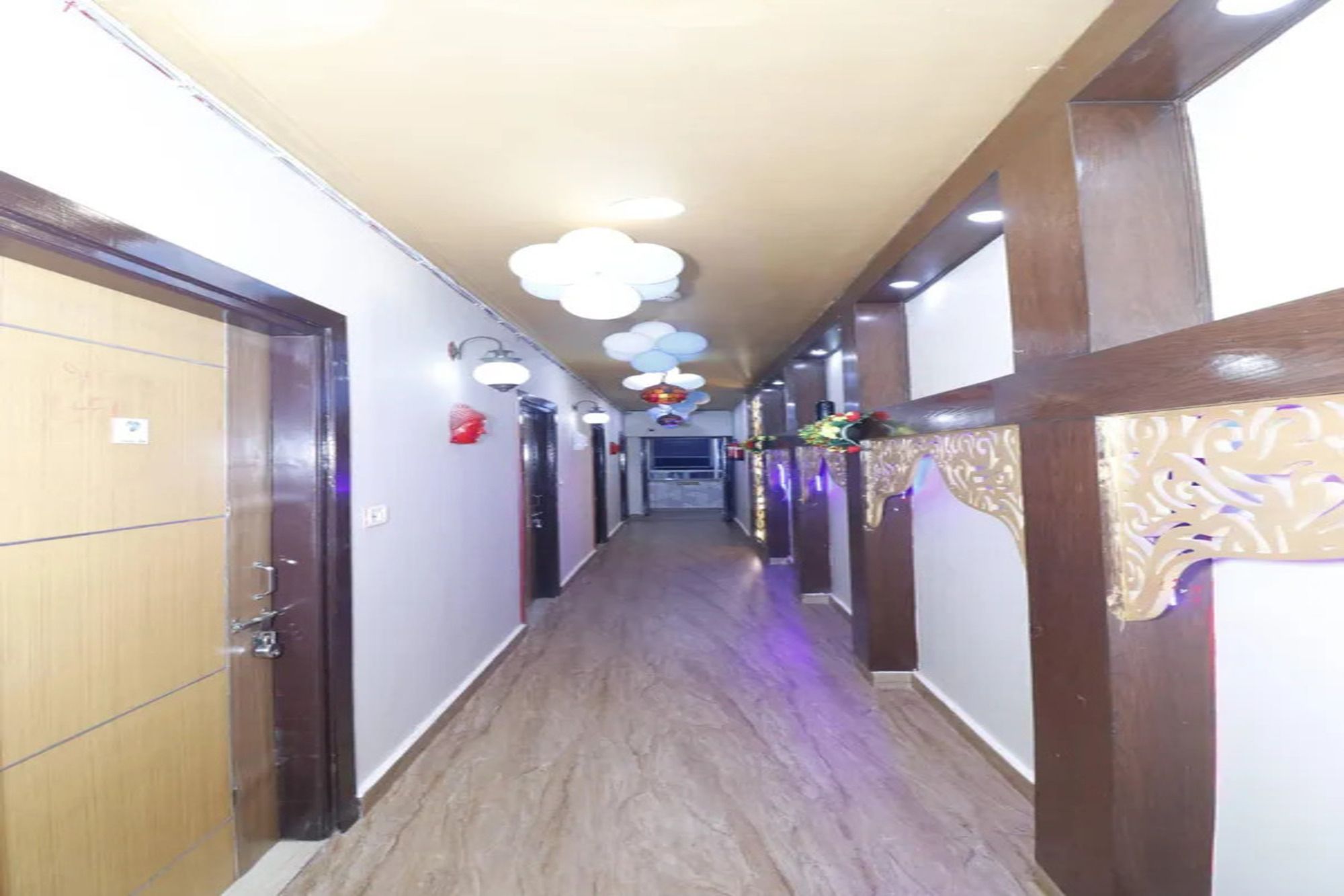 Un couloir d’hôtel avec des portes en bois sur le côté gauche, un comptoir d’accueil au bout, et un éclairage décoratif.