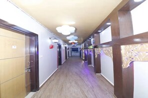 Passadís d'hotel amb portes de fusta a l'esquerra, un taulell de recepció al final i il·luminació decorativa.