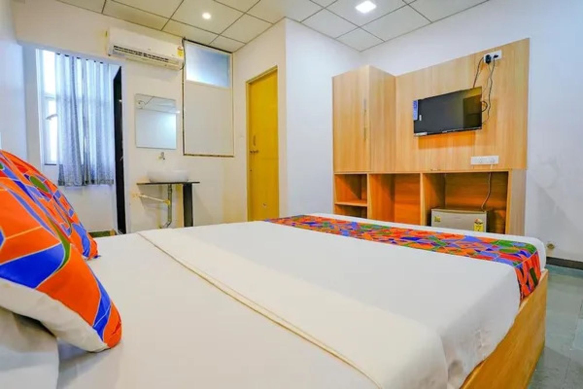 A hotel room with a bed, a television mounted on the wall, a small table, and a window with curtains.