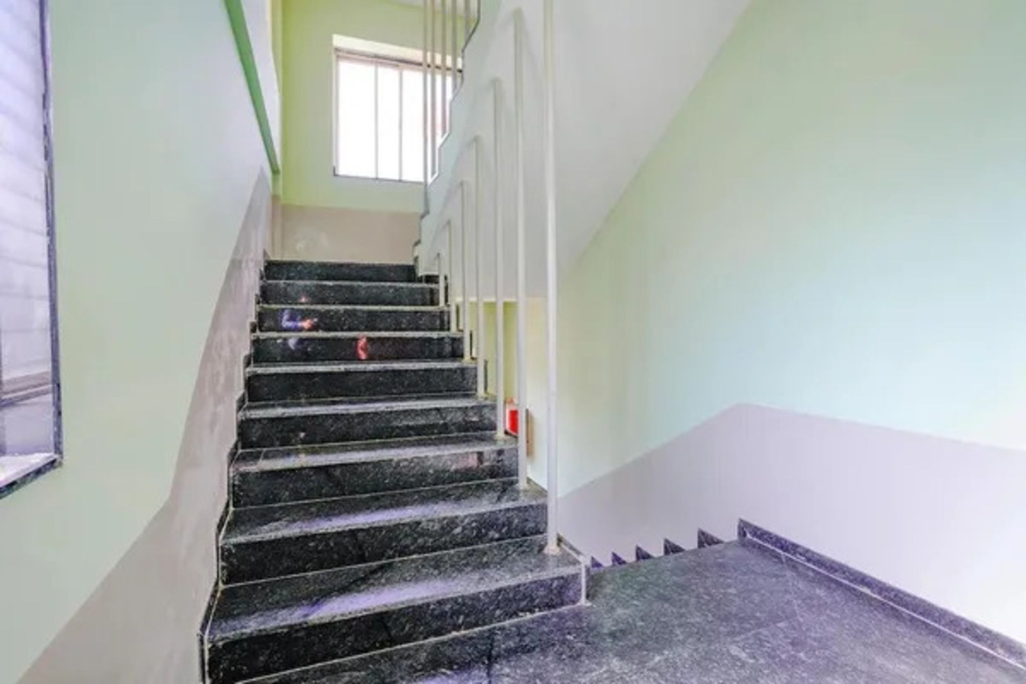 Una escalera con barandilla que lleva a un rellano con ventana.