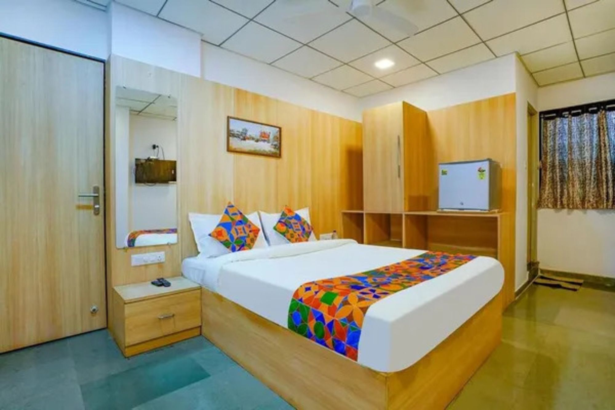 A hotel room with a bed, bedside table, wardrobe, and a small desk with a chair.