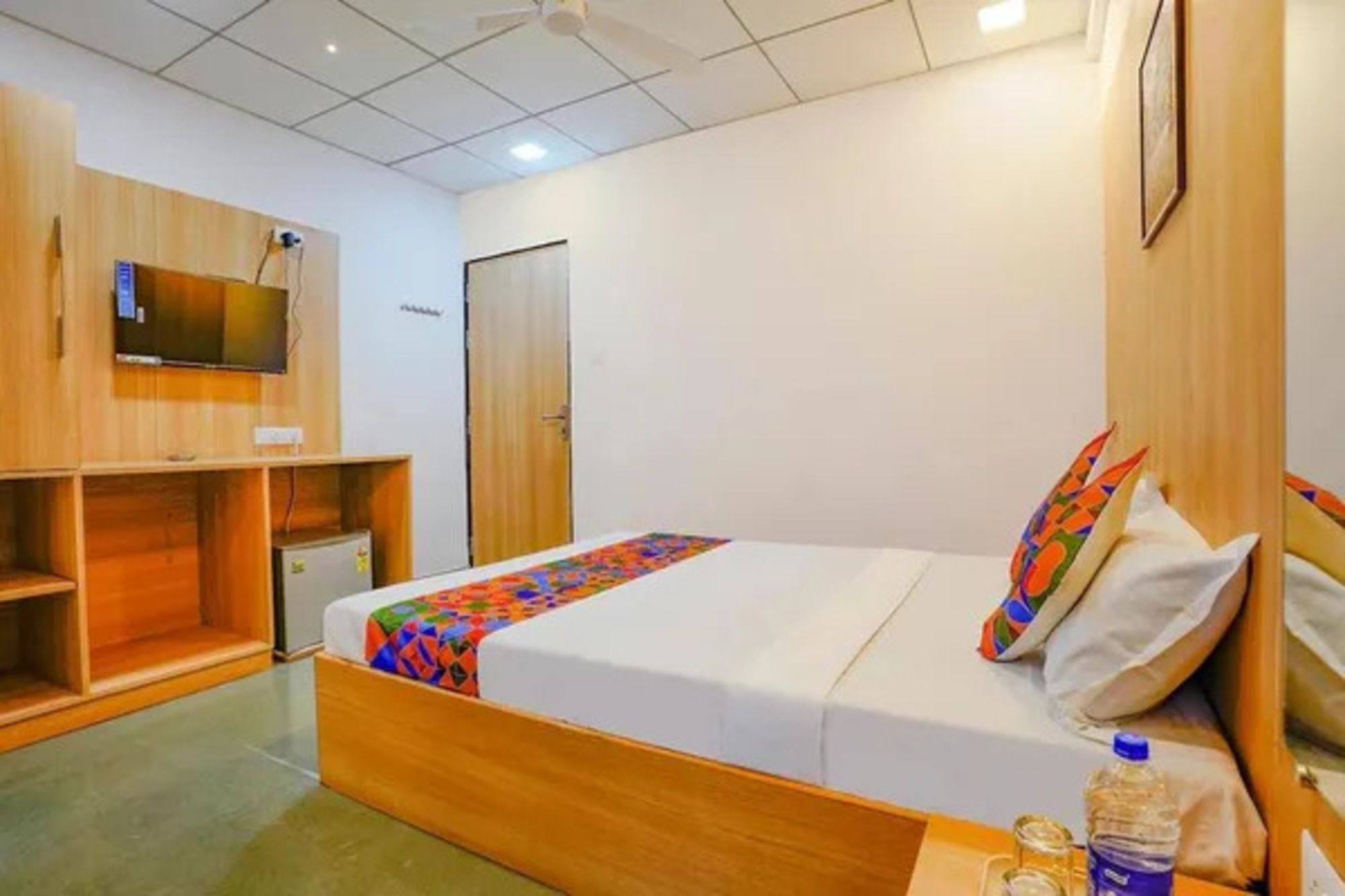 Habitación de hotel con cama, televisor, armario y escritorio con una botella de agua.