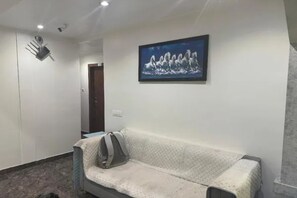 A room with a sofa, a framed picture on the wall, and a door in the background. - FabHotel Sahara Residency (Mumbai)