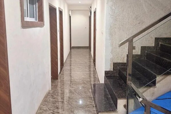 Un pasillo con piso de mármol que conduce a una escalera con barandilla de cristal.