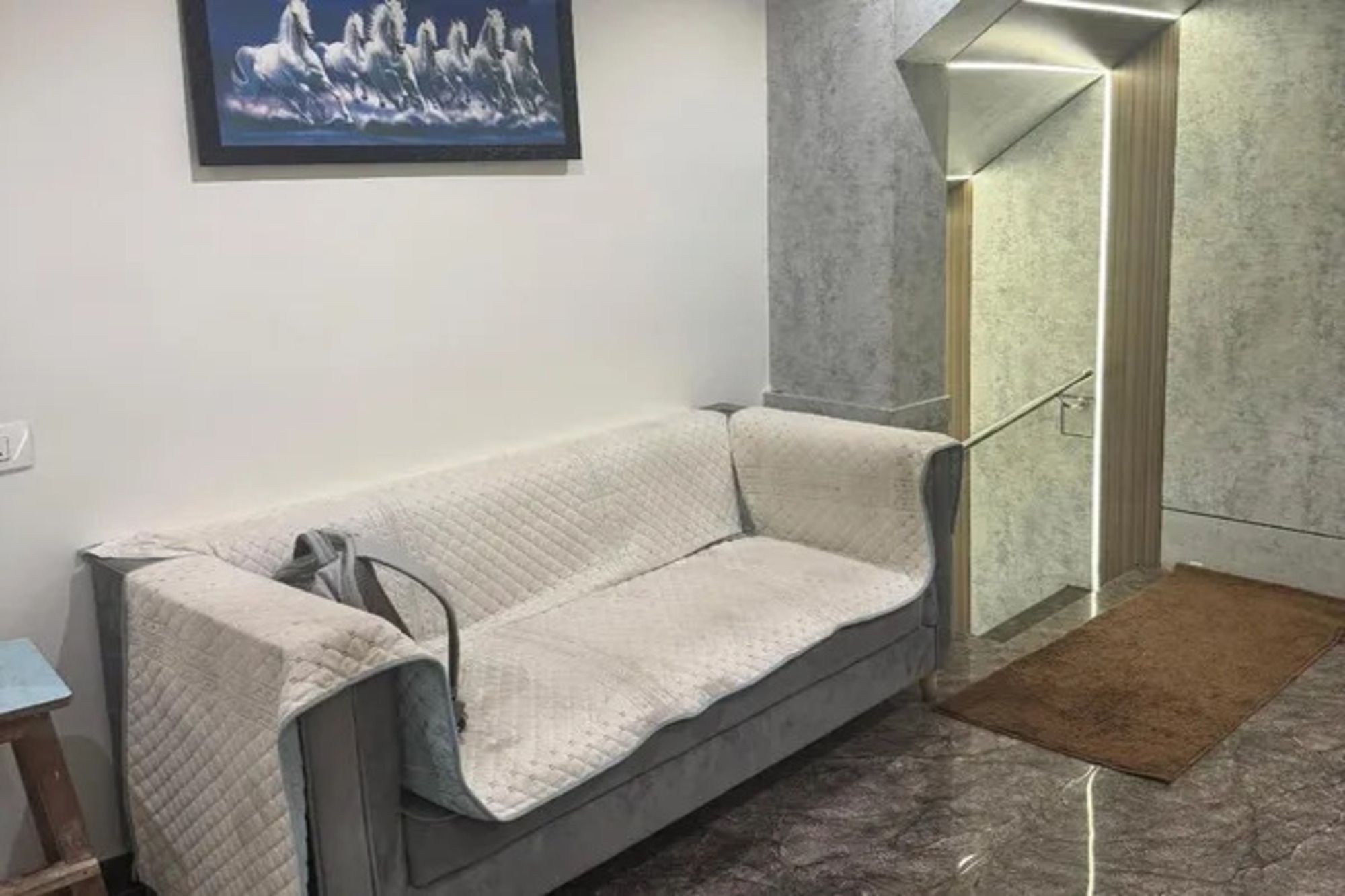 Una habitación con un sofá gris, un cuadro en la pared y una zona de ducha con puerta de cristal.