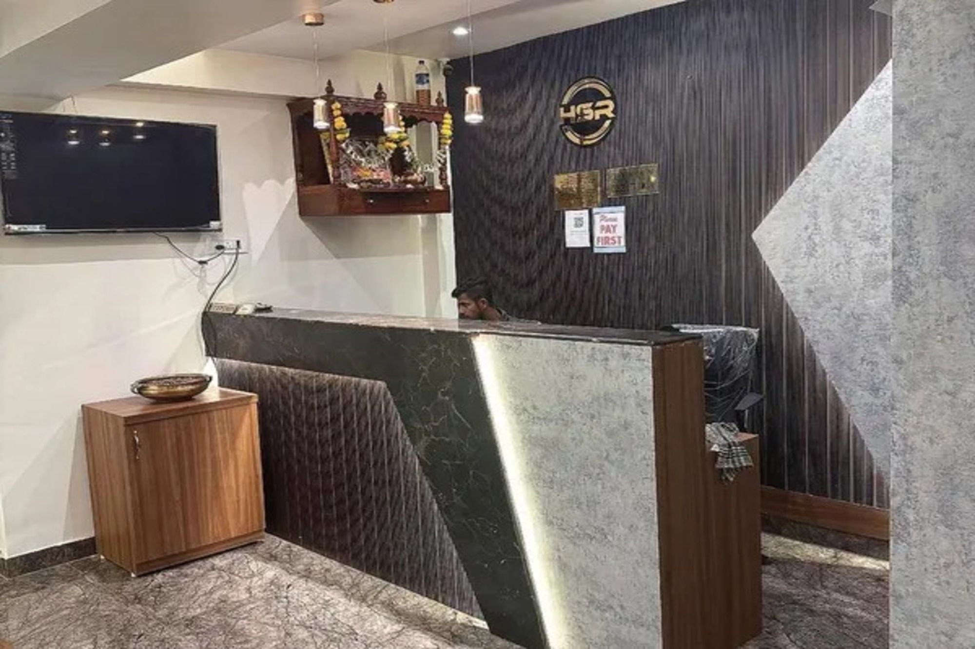 Un área de recepción con un mostrador de mármol, un mueble de madera, un televisor de pantalla plana montado en la pared y un cartel en la pared.