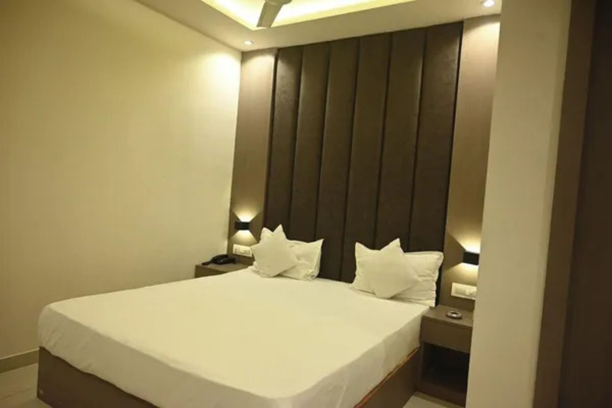 Un dormitorio con una cama grande, cabecera con listones verticales, lámparas de noche y mesita de noche.