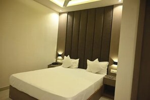 A bedroom with a large bed, a headboard with vertical slats, bedside lamps, and a nightstand. - FabHotel Sahara Residency (Mumbai)