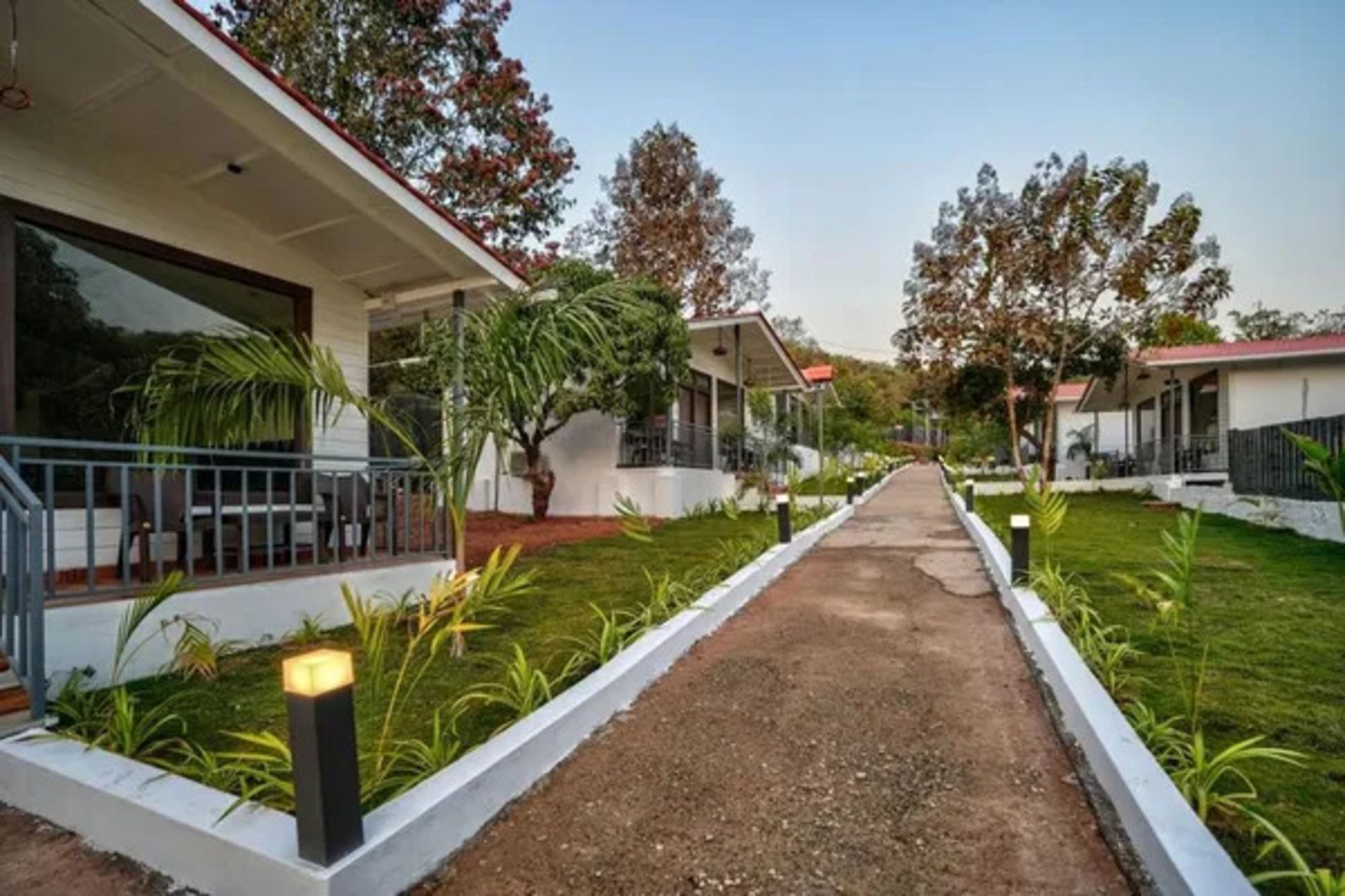 Camí cap a un edifici amb porxo i un petit jardí amb plantes.