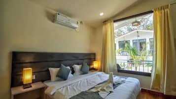 A hotel room with a bed, bedside lamps, an air conditioning unit, and a window with curtains.