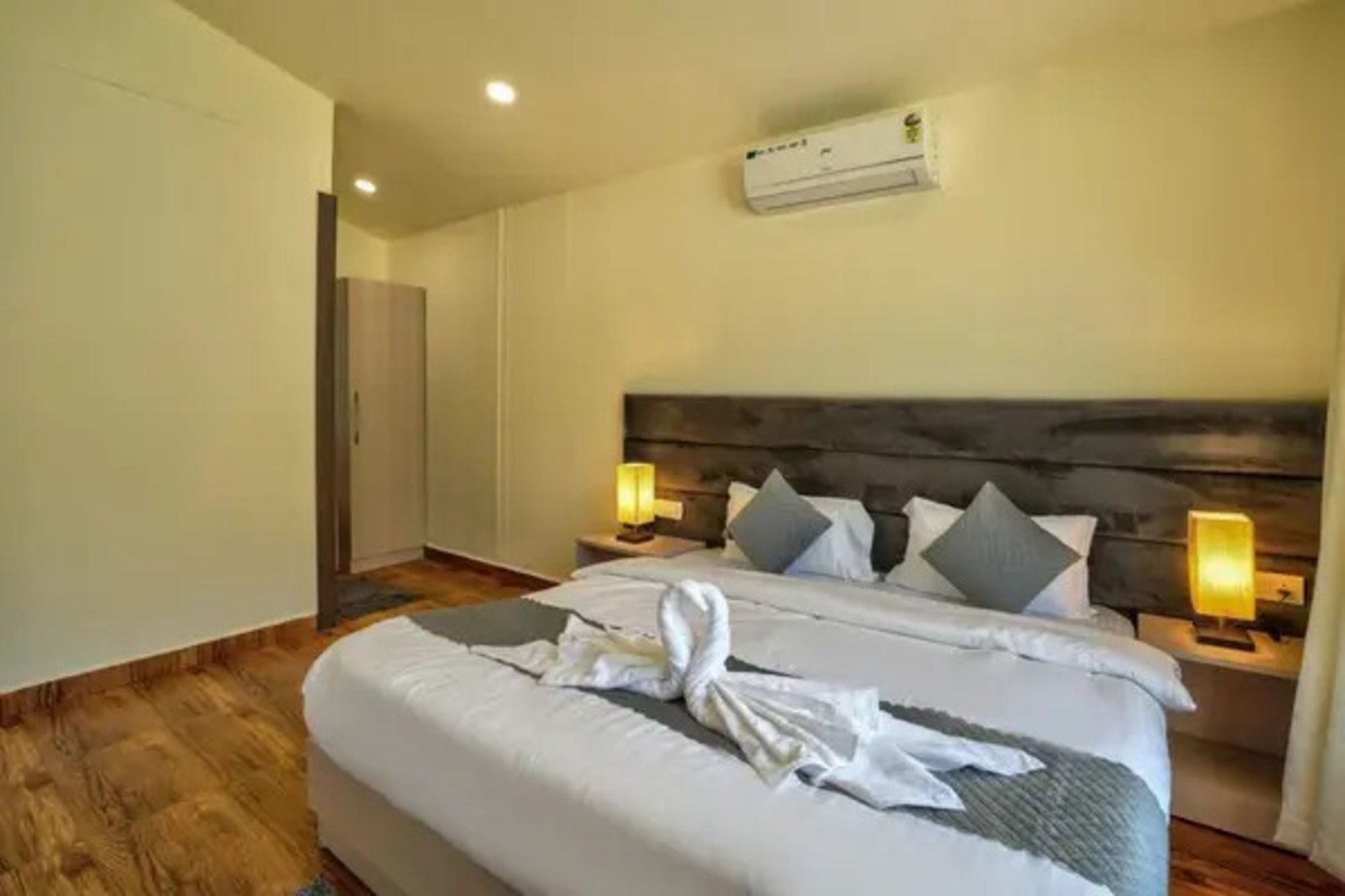 A hotel room with a bed, bedside lamps, an air conditioning unit, and a wardrobe.