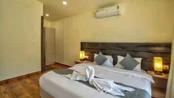 A hotel room with a bed, bedside lamps, an air conditioning unit, and a wardrobe.