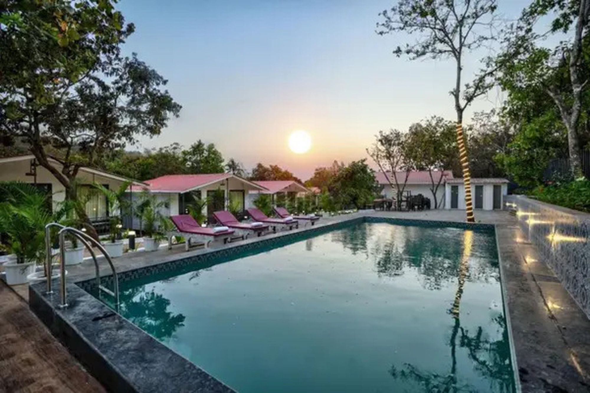 A swimming pool with lounge chairs and a sunset in the background.