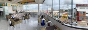 Ein Restaurant mit mehreren Tischen, Stühlen, einer Küche und großen Fenstern mit Blick auf die Stadt.