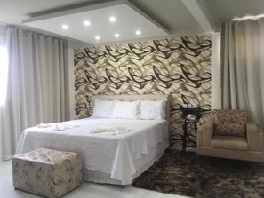 Ein Schlafzimmer mit einem Bett, einem Sessel, einem kleinen Tisch und einer Wand mit Muster.