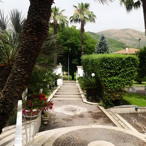 Un chemin menant à un bâtiment doté d’un jardin aménagé, de palmiers et offrant une vue sur des collines.