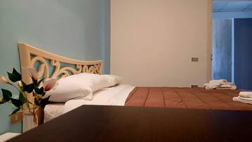 A bedroom with a wooden bed, white bedding, a vase with flowers, and a blue wall.