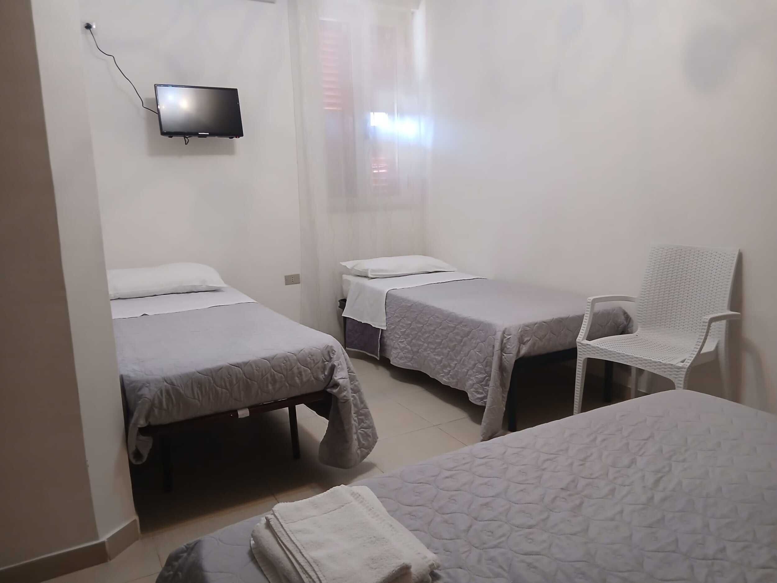 A room with two beds, a chair, and a television mounted on the wall.