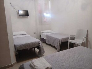 A room with two beds, a chair, and a television mounted on the wall.