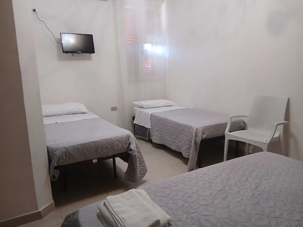 Une chambre avec deux lits, une chaise et un téléviseur fixé au mur.