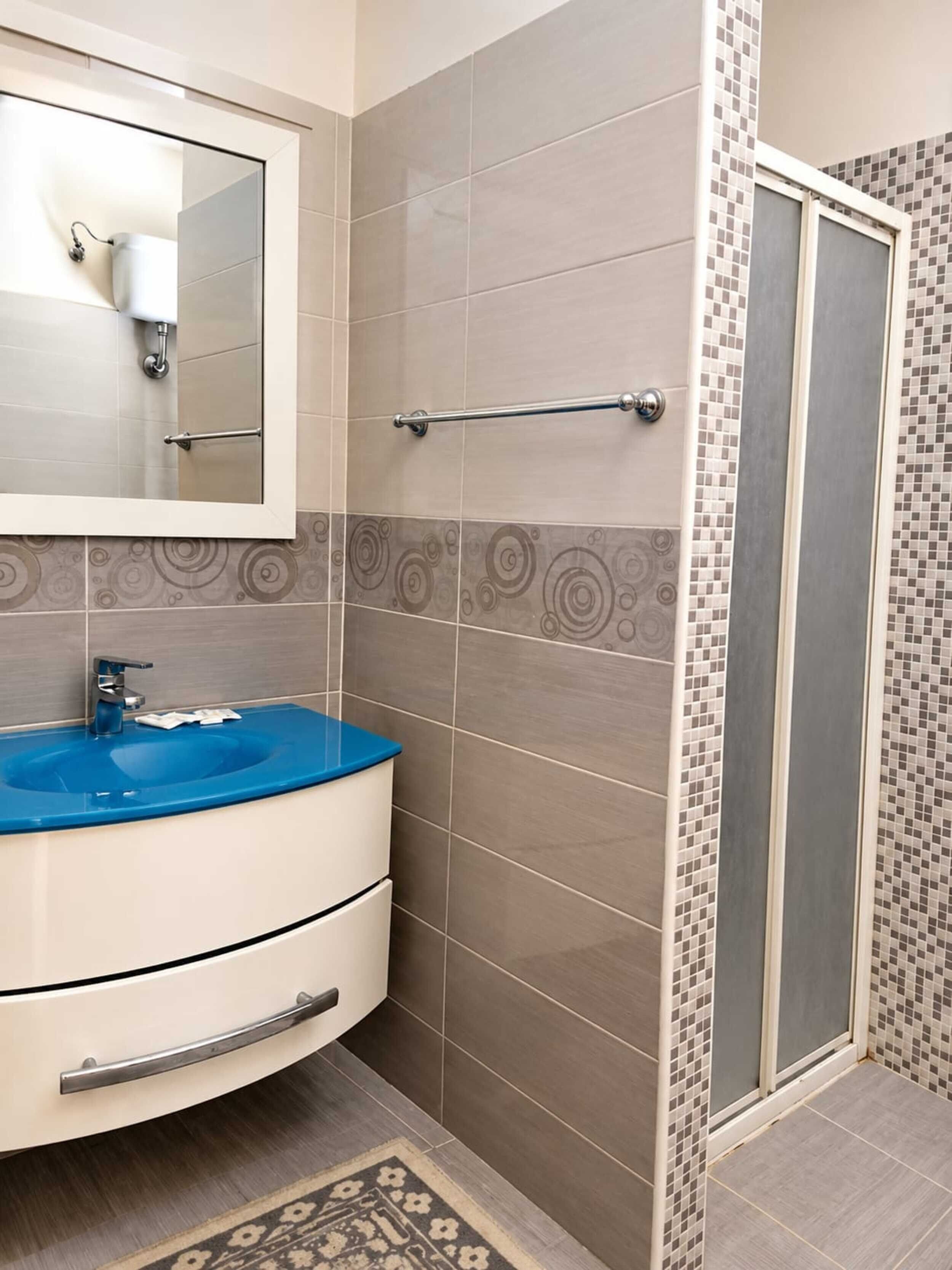 A bathroom with a blue sink, a mirror, and a shower area.