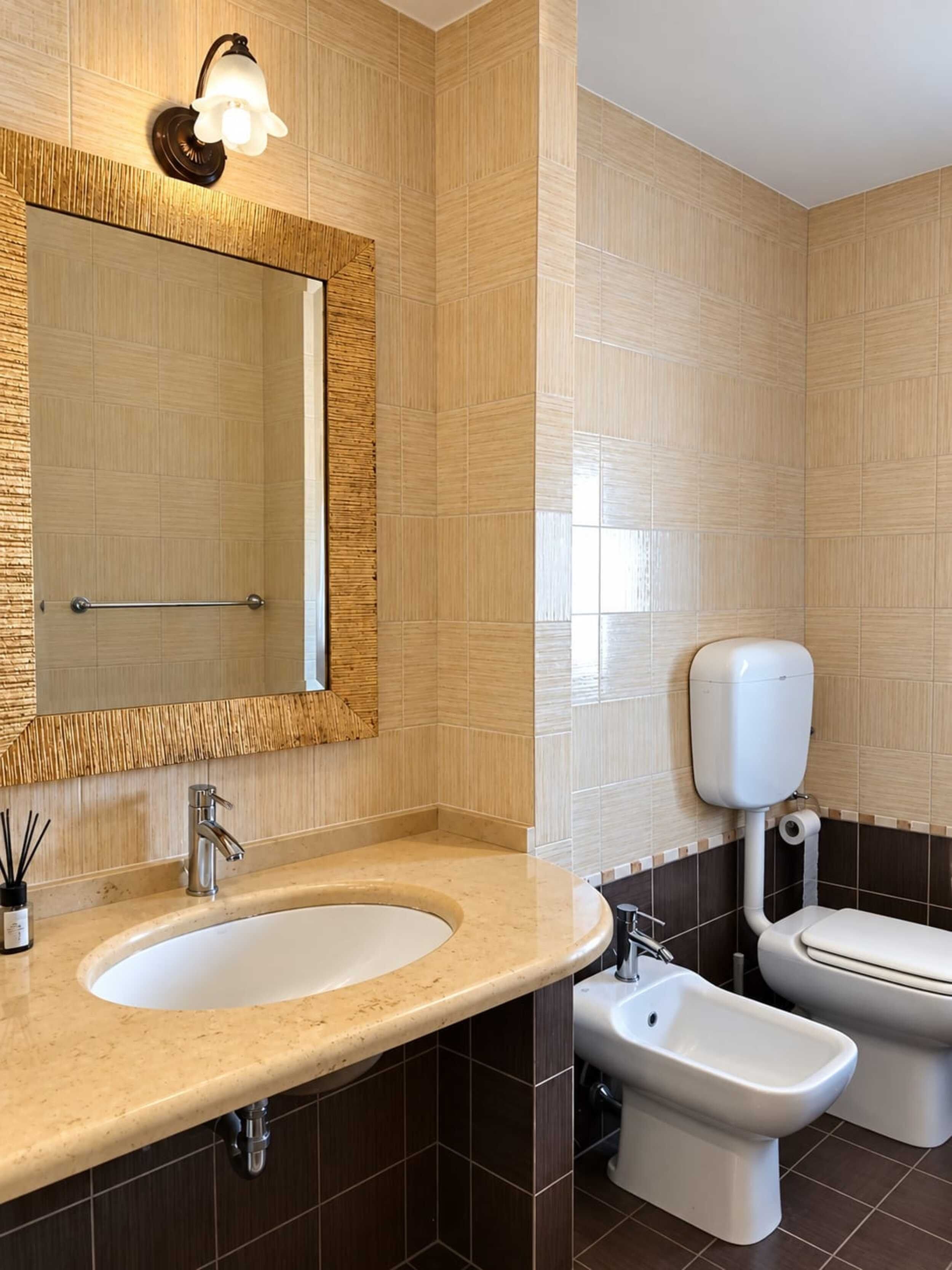 A bathroom with a sink, mirror, bidet, toilet, and a wall-mounted light fixture.