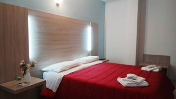 A hotel room with a bed, a bedside table, a nightstand, a vase with flowers, and a wall-mounted light.