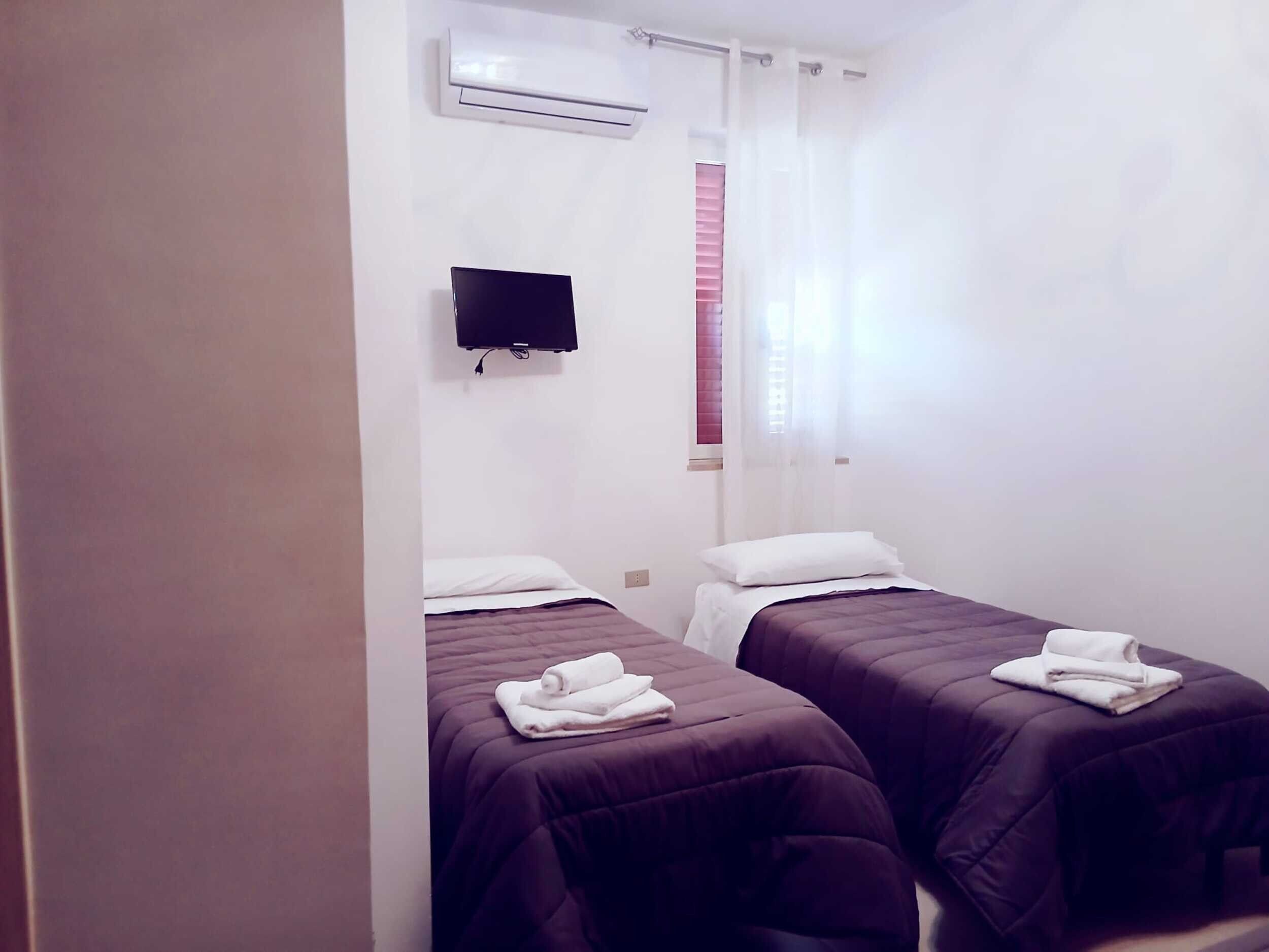 Una habitación de hotel con dos camas, un equipo de aire acondicionado, un televisor y una ventana con cortinas.