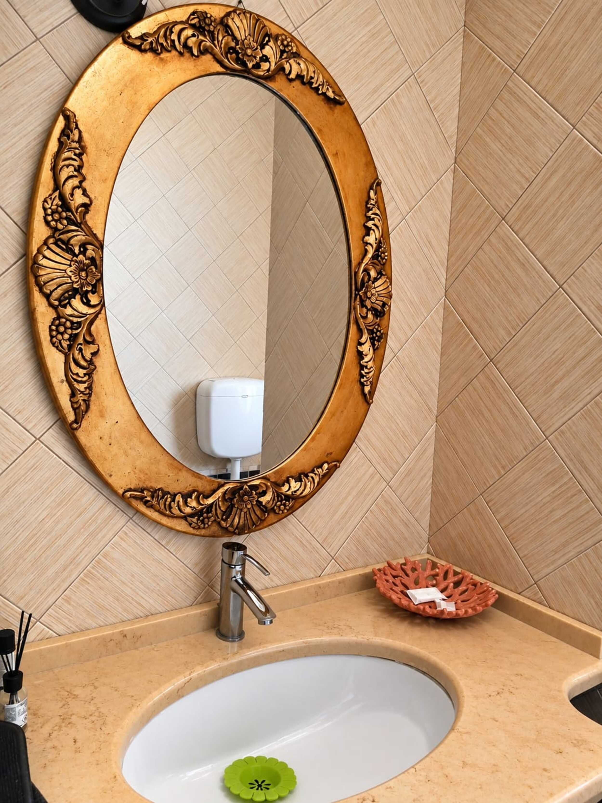 Un baño con lavamanos, espejo con marco ornamentado y dispensador de jabón.