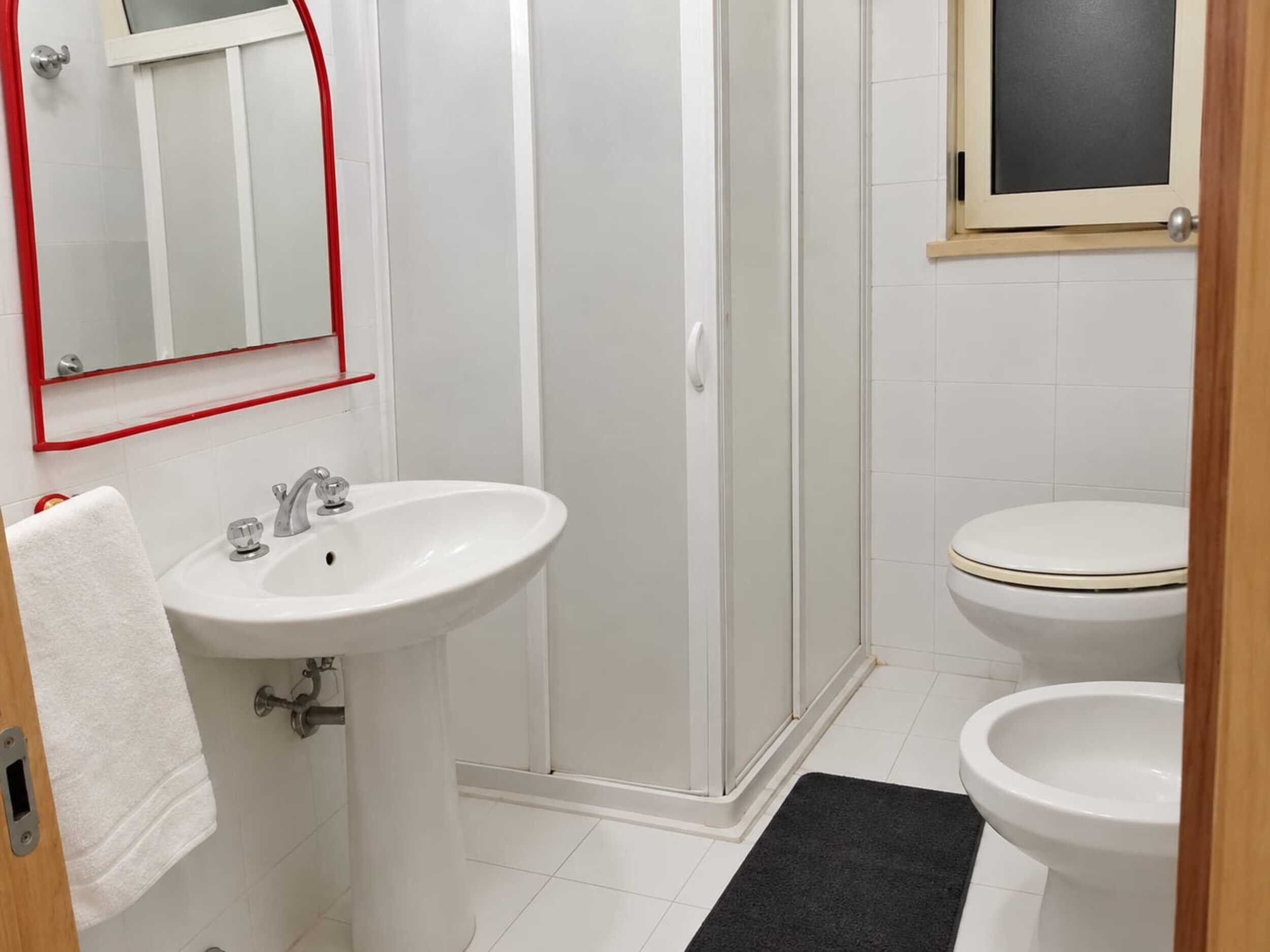 Une salle de bain avec un lavabo blanc, une douche en verre et deux toilettes.