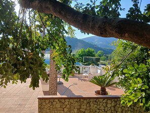 Eine Terrasse mit Steinmauern, Kübelpflanzen, Gartenmöbeln und Blick auf die umliegende Landschaft.