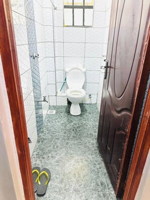 A bathroom with a toilet, a shower area, and a pair of flip-flops on the floor. - Lulu Nest studio Umoja (Nairobi)