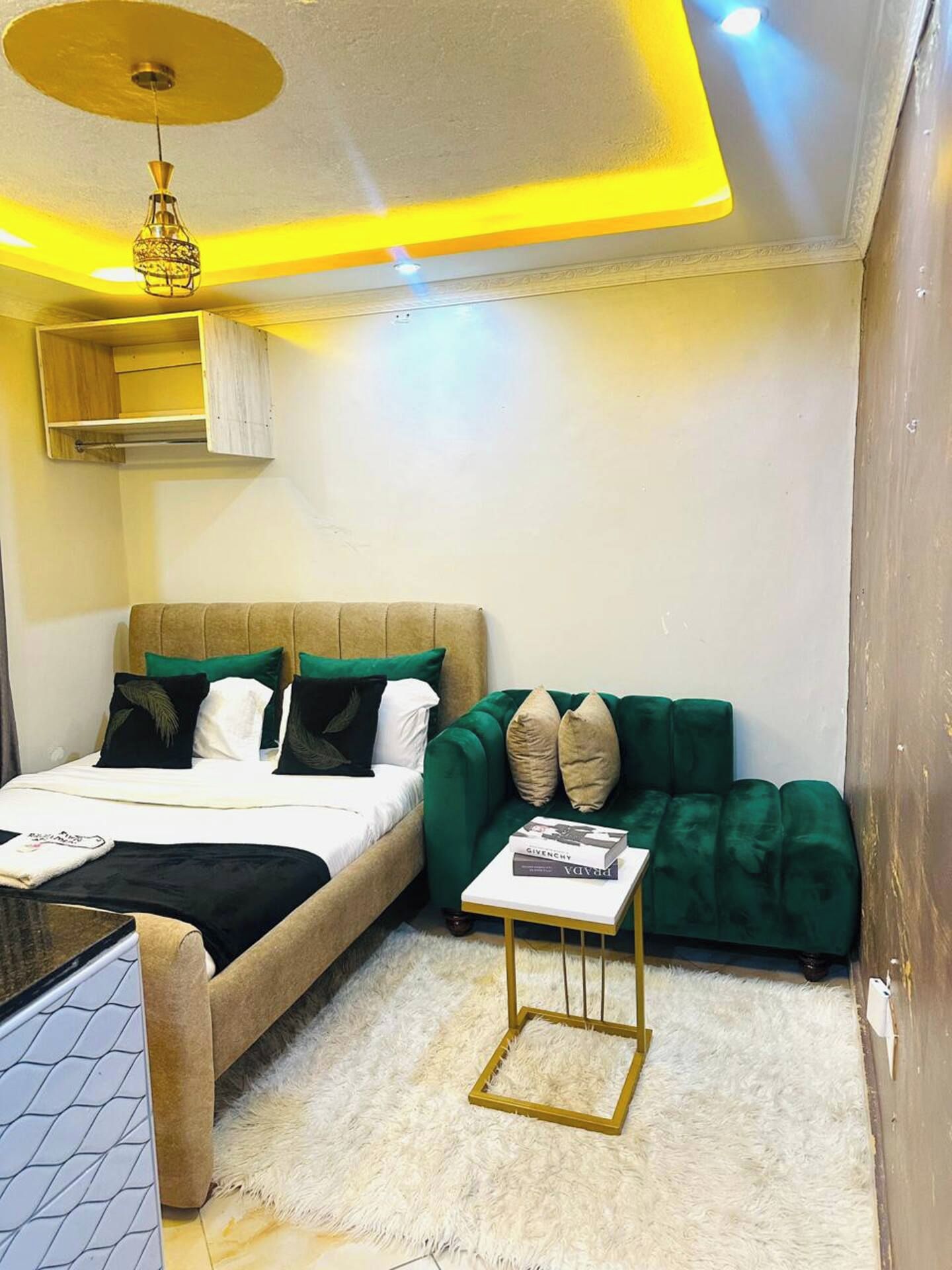 A bedroom with a bed, a green sofa, a small table, and a ceiling light fixture.