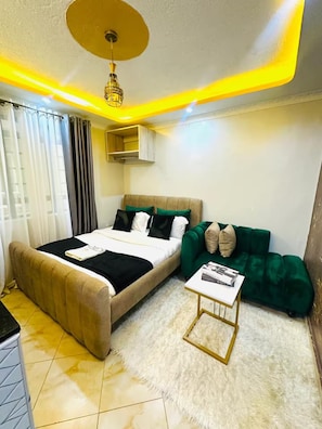 A bedroom with a bed, bedside table, green sofa, and a ceiling light fixture. - Lulu Nest studio Umoja (Nairobi)