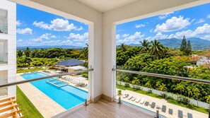 Un balcón con vistas a una piscina y abundante vegetación.