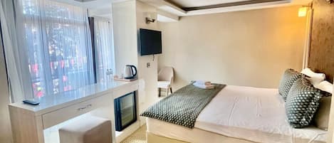 Una habitación de hotel moderna con una cama, un escritorio, una silla, un televisor y un ventanal con cortinas.