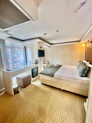 Una habitación de hotel moderna con una cama, un escritorio, una silla, un televisor y un ventanal con cortinas.