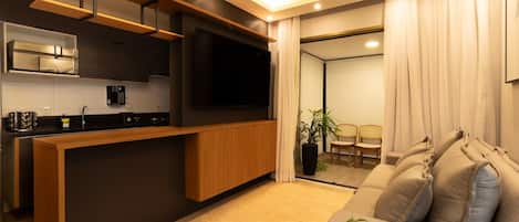 A modern living space with a kitchen, a flat-screen TV, a sofa, and a dining area.