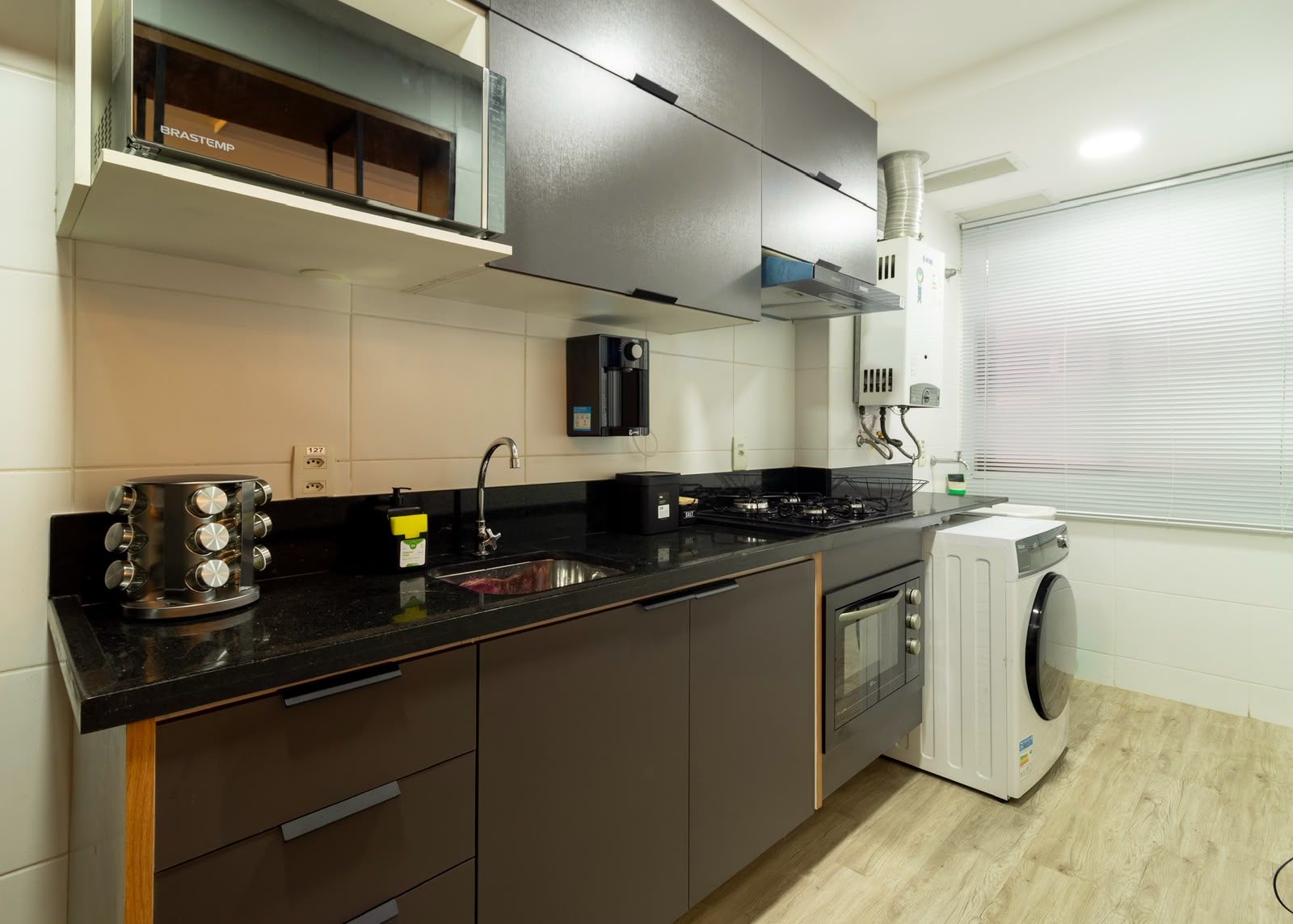 A modern kitchen with a built-in oven, a microwave, a sink, and a washing machine.