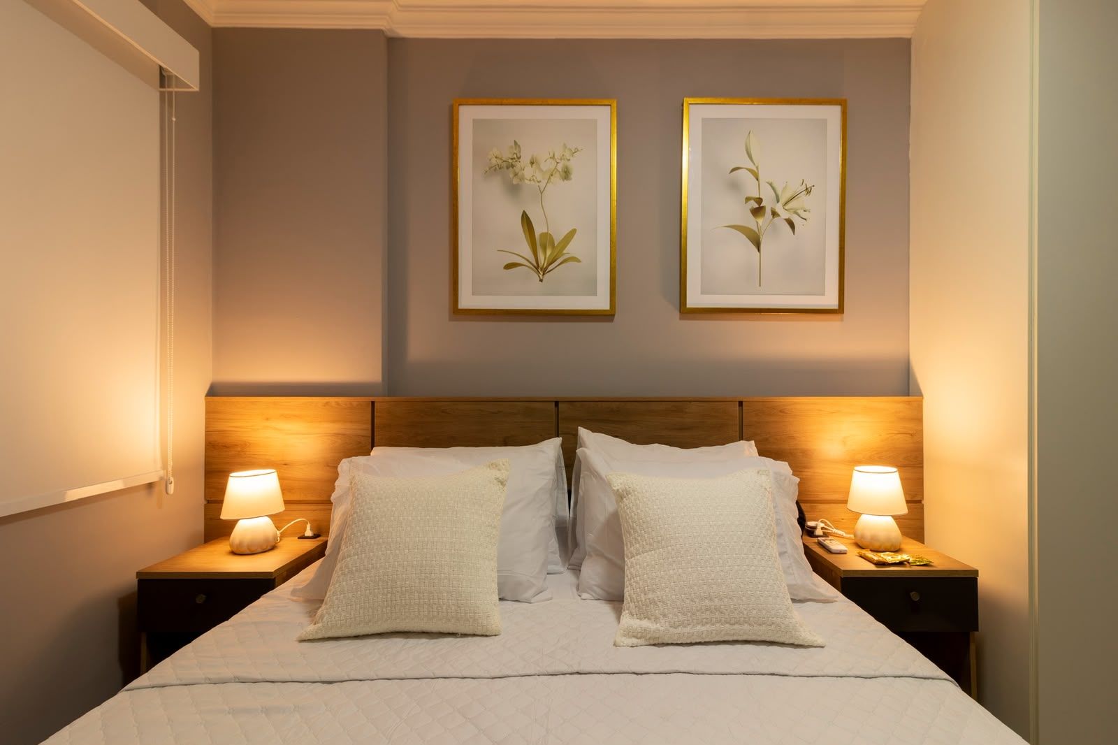 A double bed with two nightstands, each with a lamp, in a room with a wooden headboard and framed botanical prints on the wall.