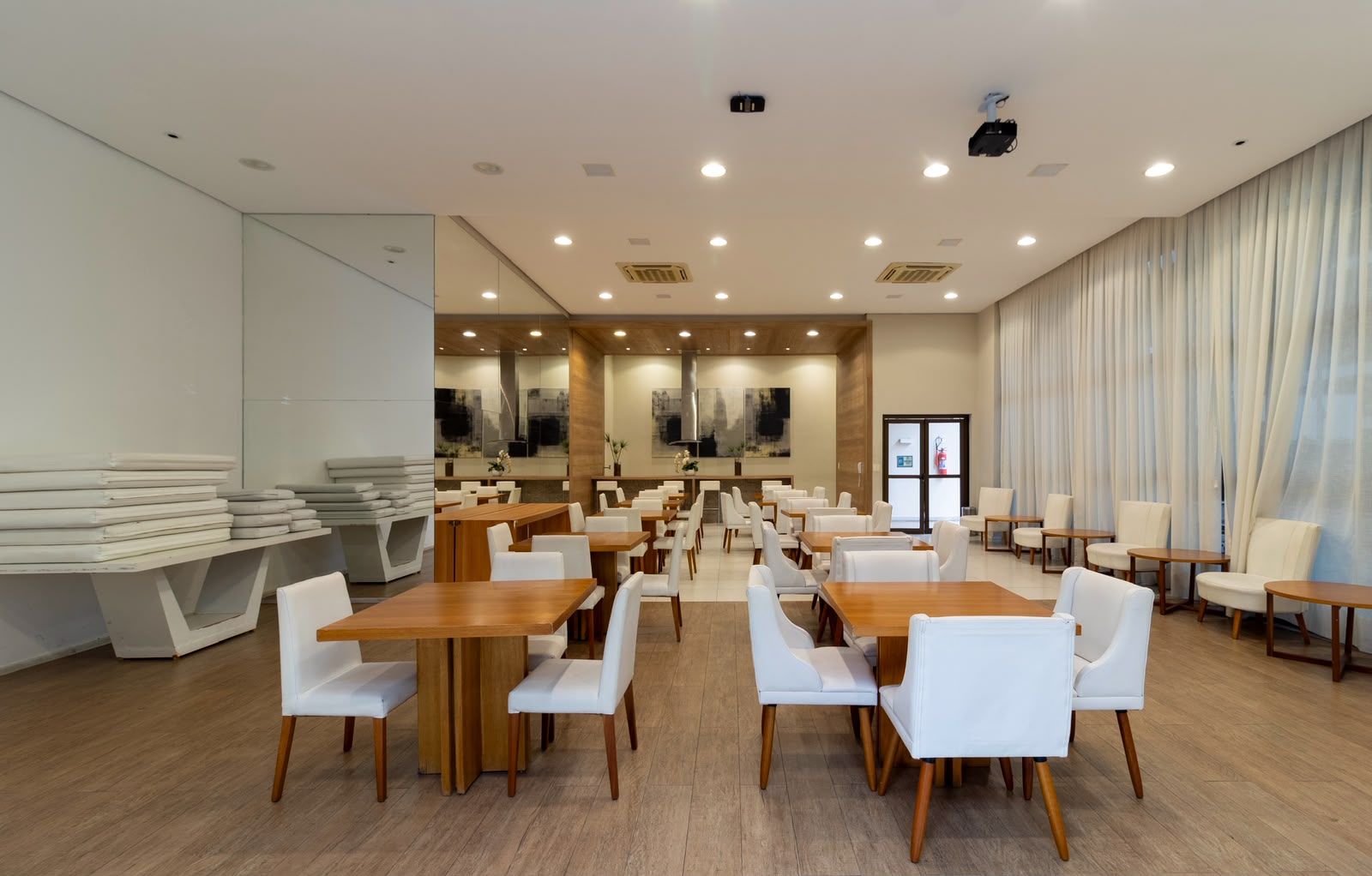 Un vaste espace dédié à la salle à manger, avec de nombreuses tables et chaises, une grande fenêtre agrémentée de rideaux et un design moderne au niveau du plafond.