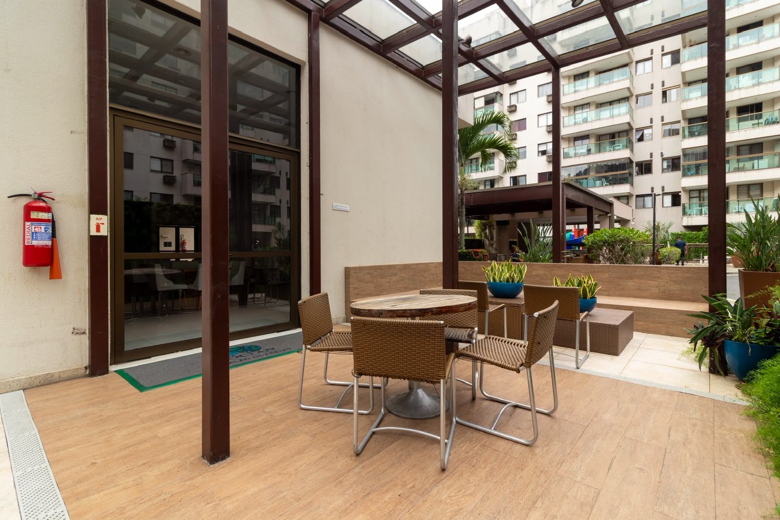 An outdoor patio area with a round table and chairs, surrounded by potted plants and a fire extinguisher.
