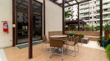 An outdoor patio area with a round table and chairs, surrounded by potted plants and a fire extinguisher.