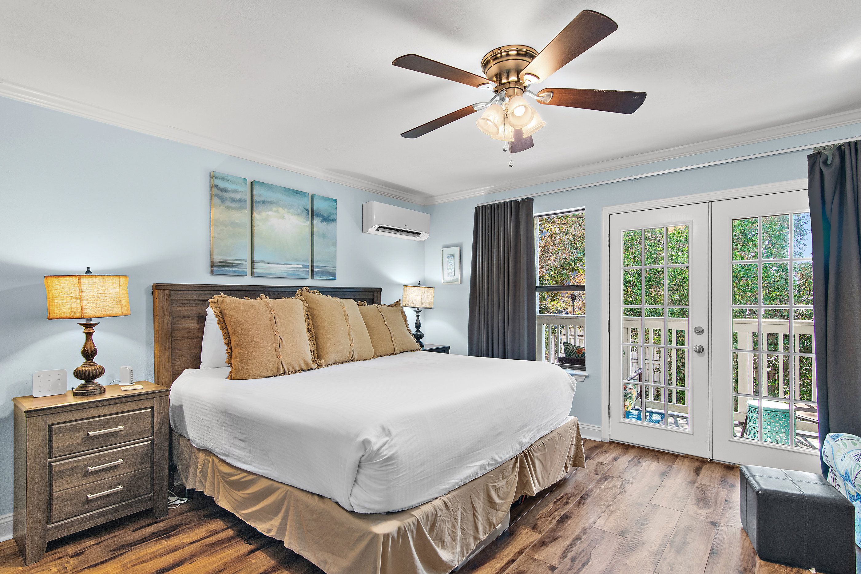 A bedroom with a bed, bedside lamps, a ceiling fan, and a view through a glass door.