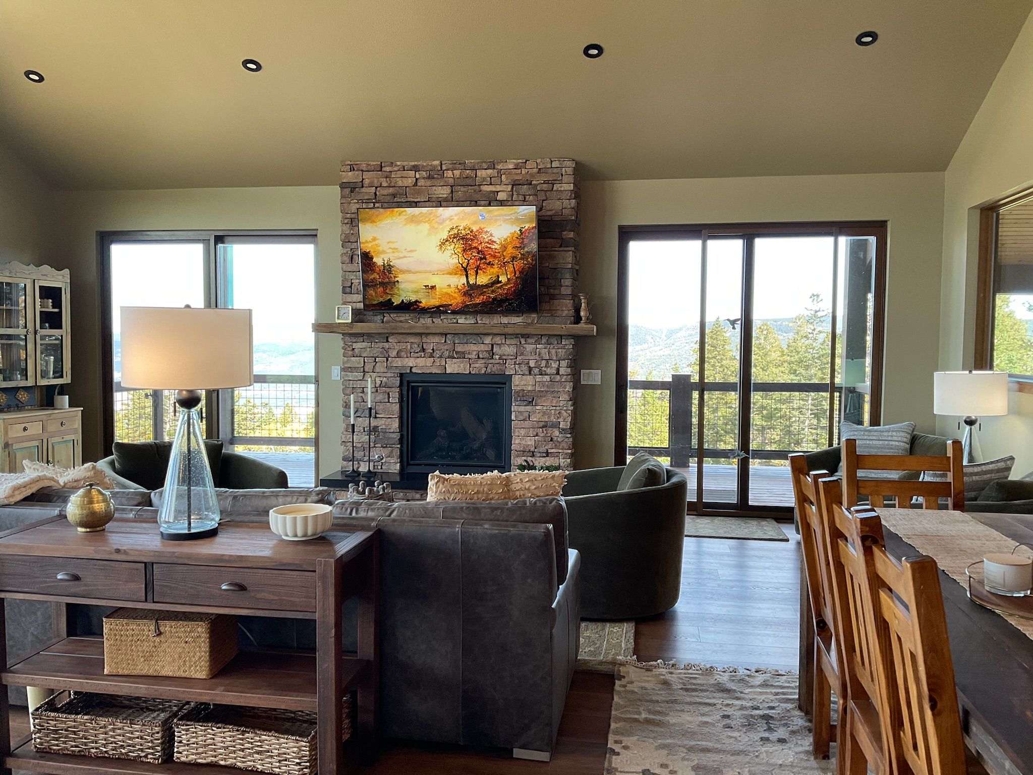 A spacious living room with a stone fireplace, comfortable seating, and large windows offering a view of the outdoors.