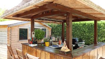 Un'area bar esterna in legno con un pergolato, posti a sedere e un barbecue.